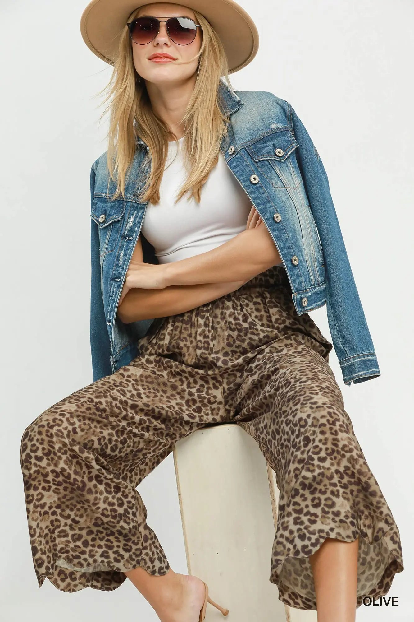 Woman wearing a denim jacket, white top, and leopard print pants on a white background