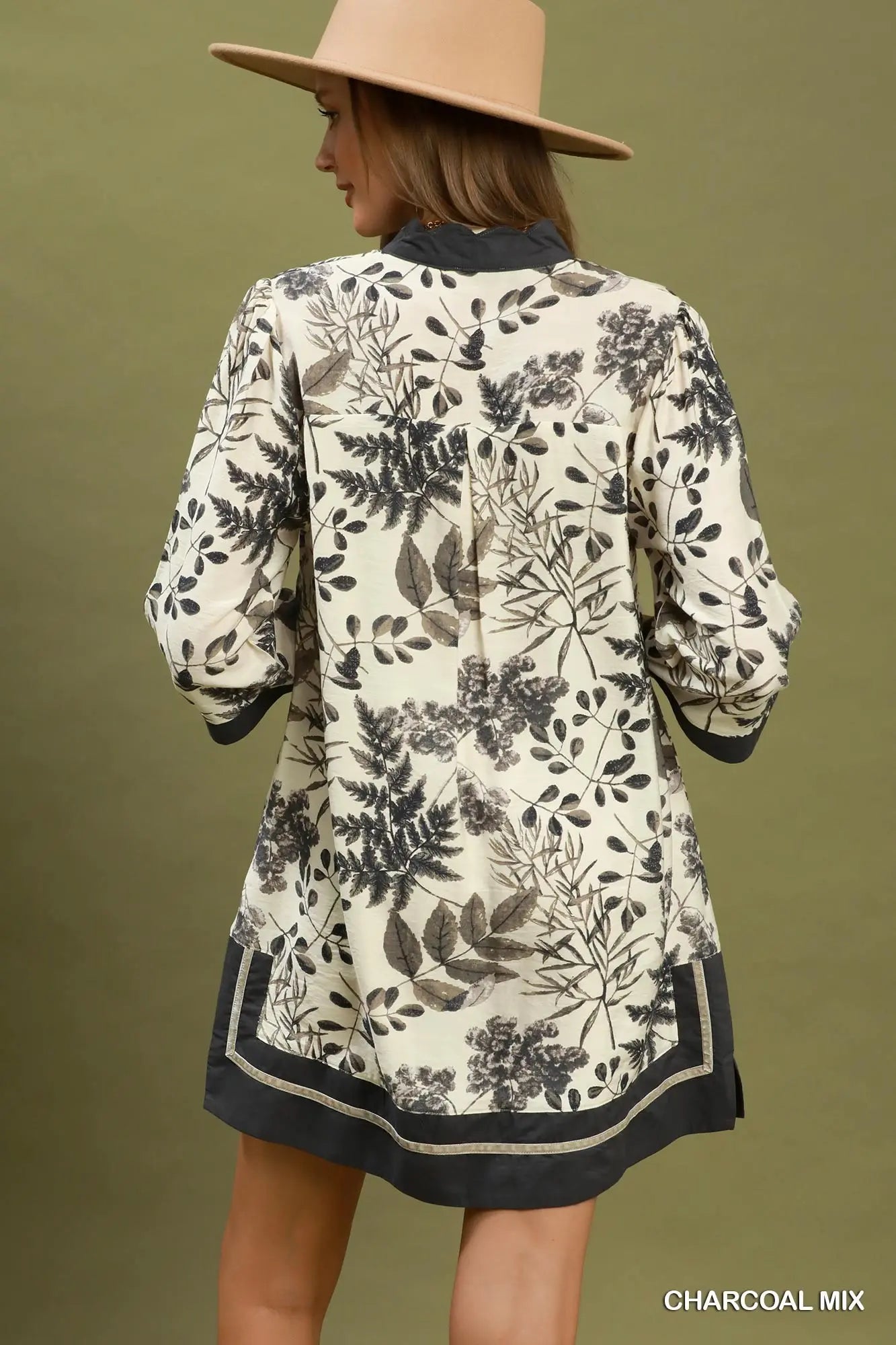 Woman wearing a floral-patterned dress with a beige hat on a green background