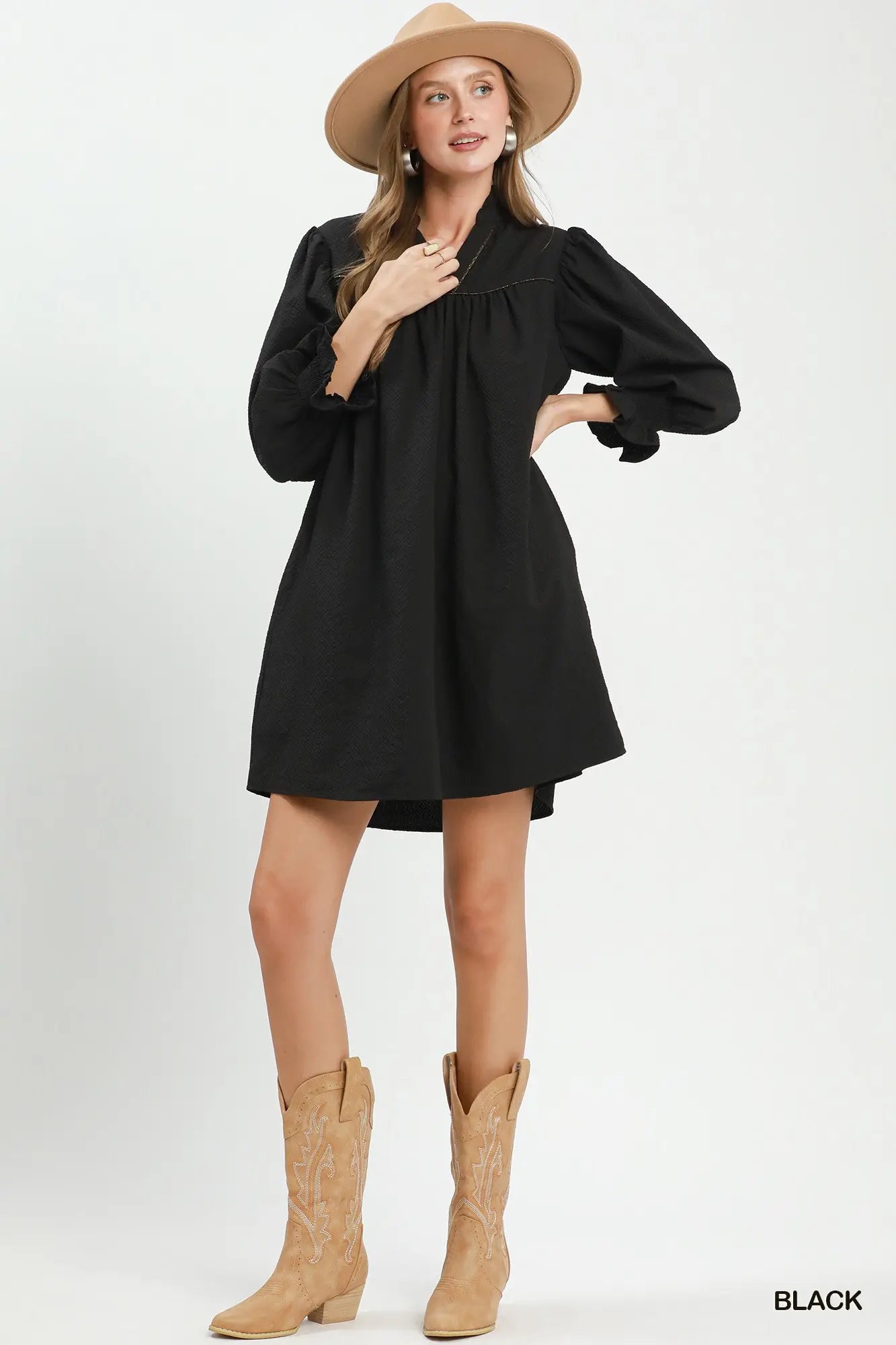 Woman wearing a black dress with puffed sleeves, beige hat, and boots on a white background