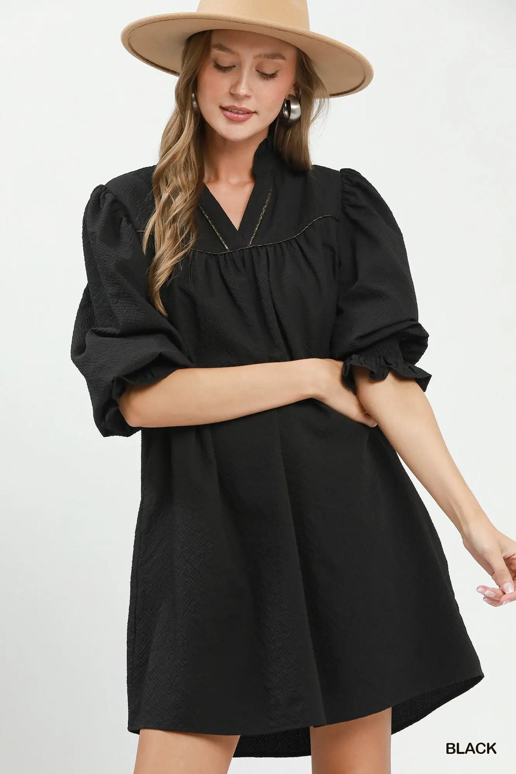 Woman wearing a black dress with puffed sleeves and a beige hat on a white background