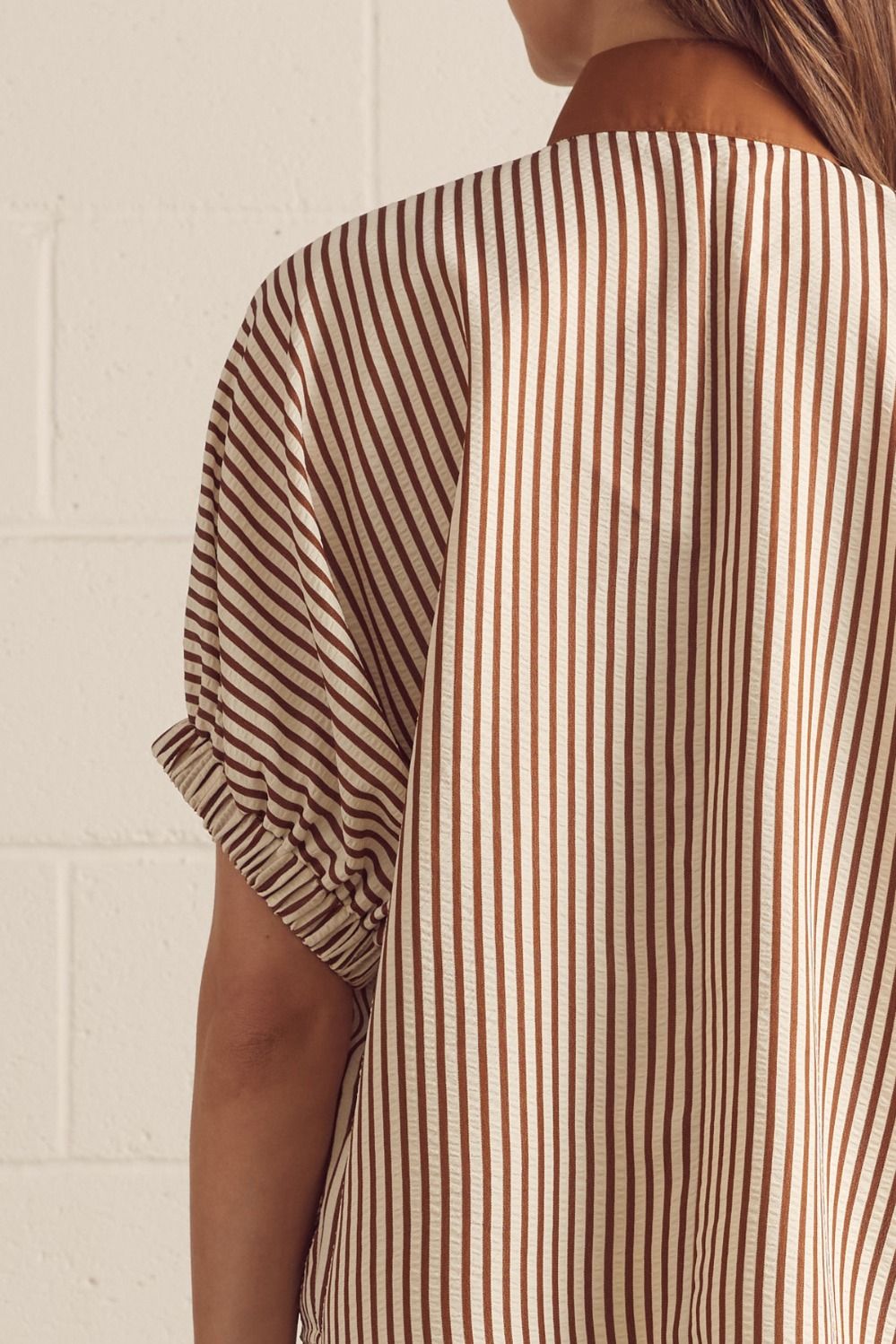 Close-up of a person wearing a brown and beige striped shirt against a white brick wall.