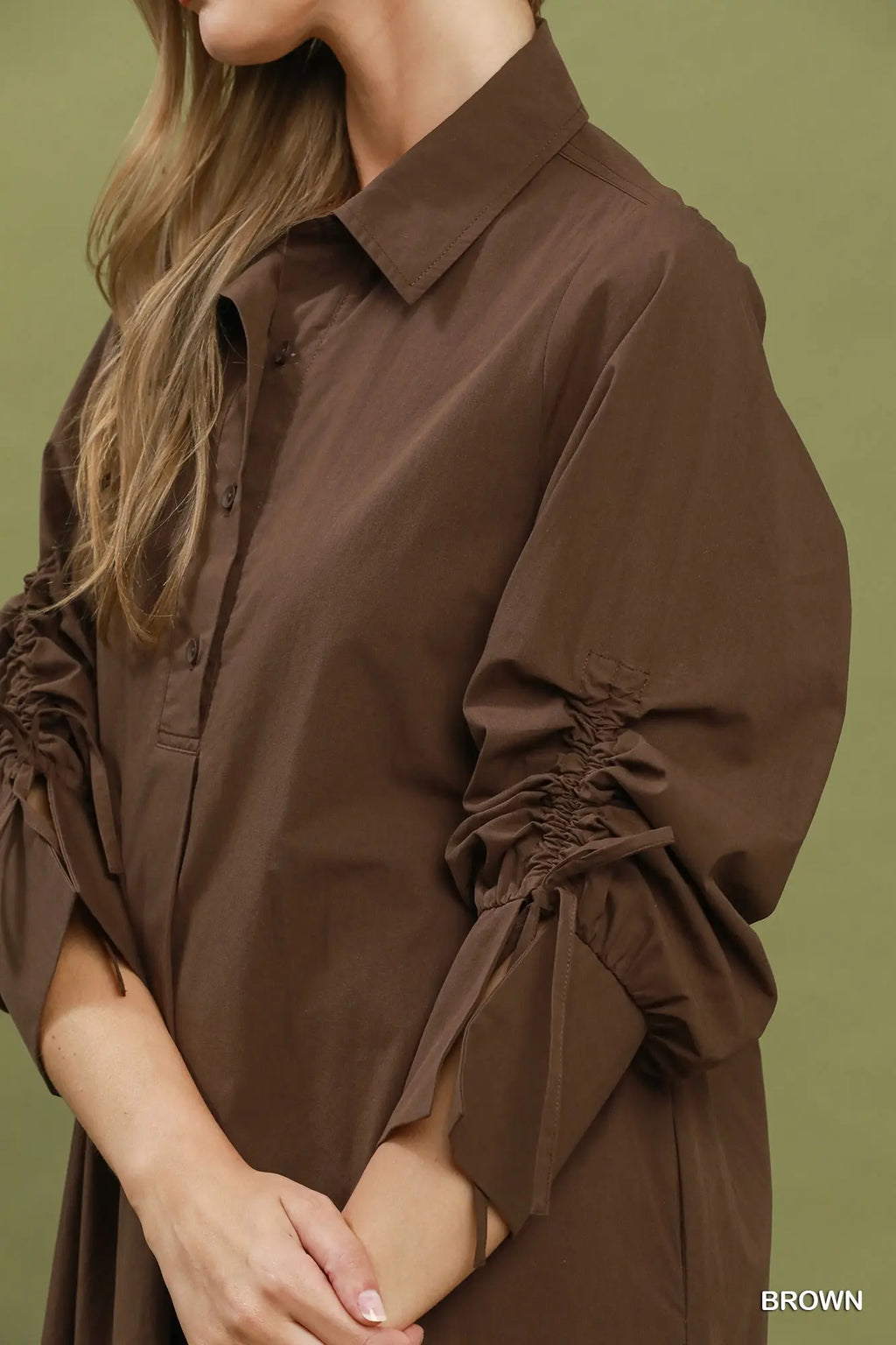 Brown shirt with ruffled sleeves on a person against a green background