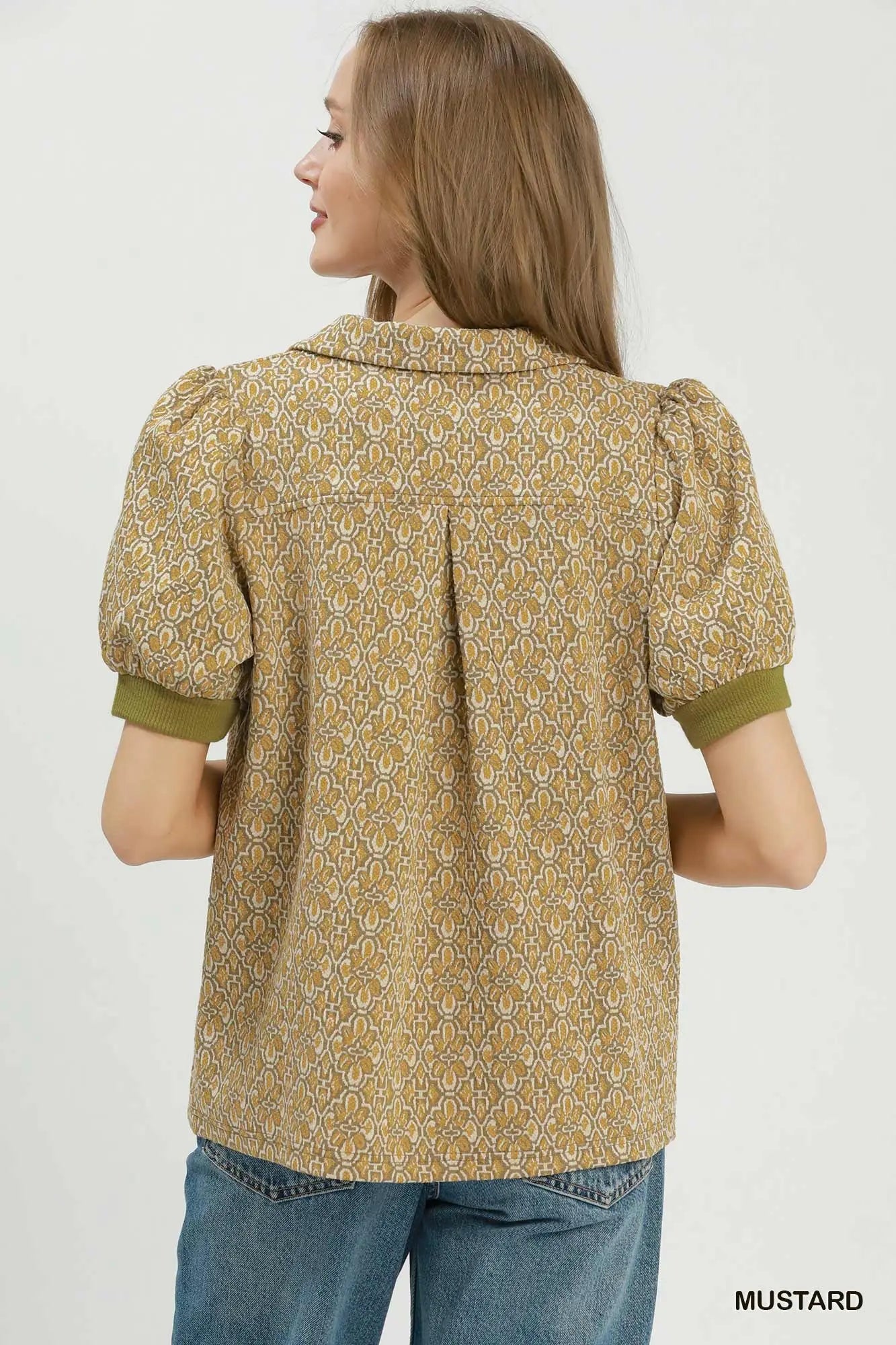 Woman wearing a mustard yellow patterned blouse with puff sleeves on a white background