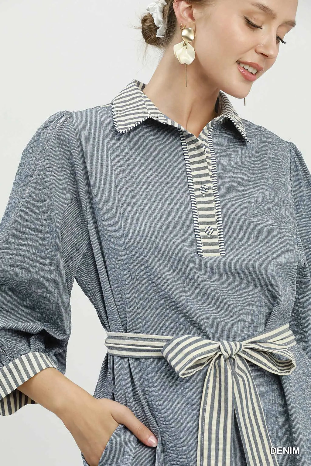 Woman wearing a denim dress with striped collar and belt on a white background