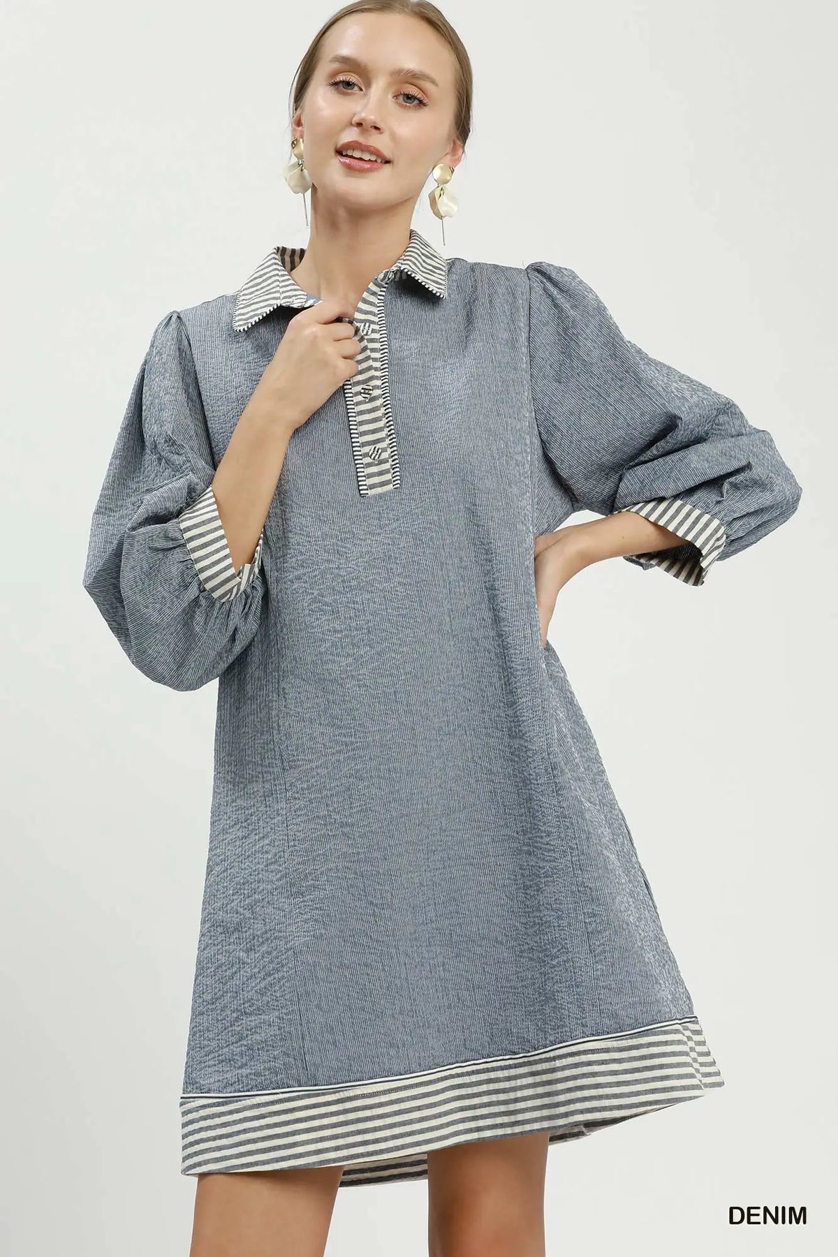 Woman wearing a denim dress with striped cuffs and collar on a white background
