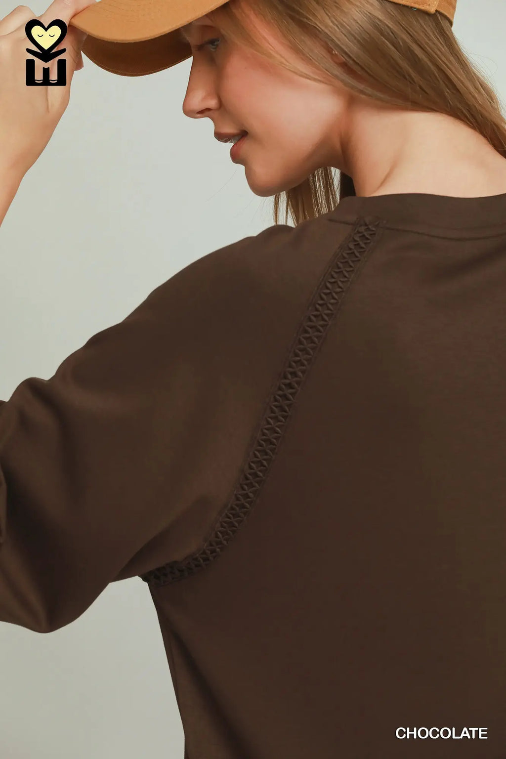 Woman wearing a brown top with braided details and a beige hat on a neutral background