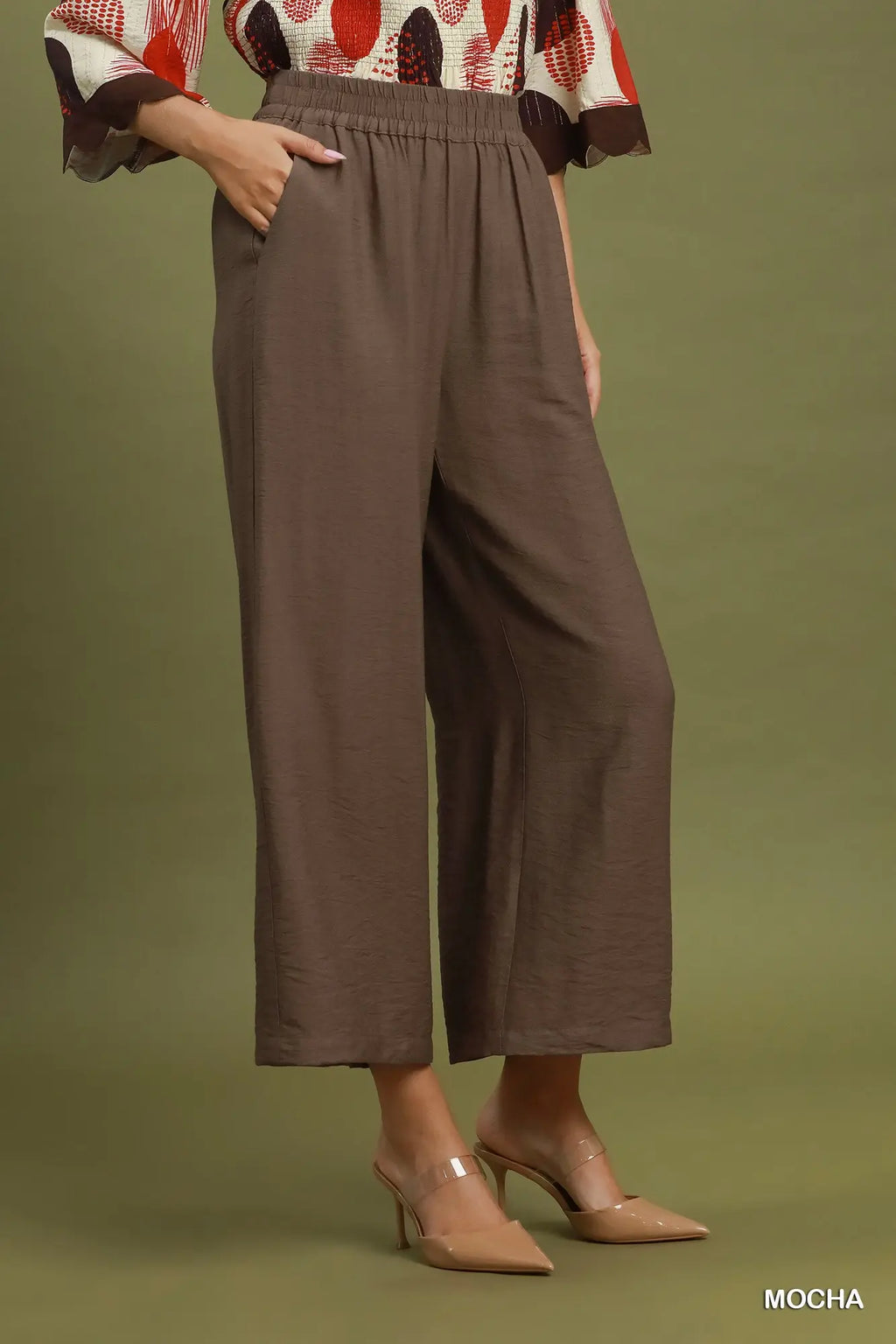 A model is shown from the waist down wearing a pair of wide-leg cropped trousers in a solid mocha brown color. The pants feature an elastic waistband and side pockets.