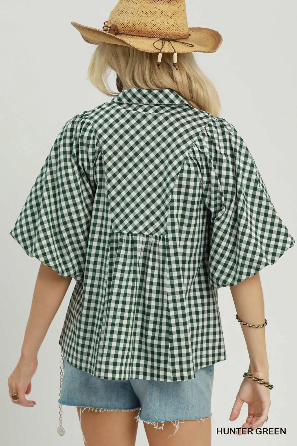 A woman shown from the back wearing a green and white gingham short-sleeve blouse with a gathered waist seam, paired with denim shorts and a straw hat. The color label 'HUNTER GREEN' is visible in the bottom right corner.