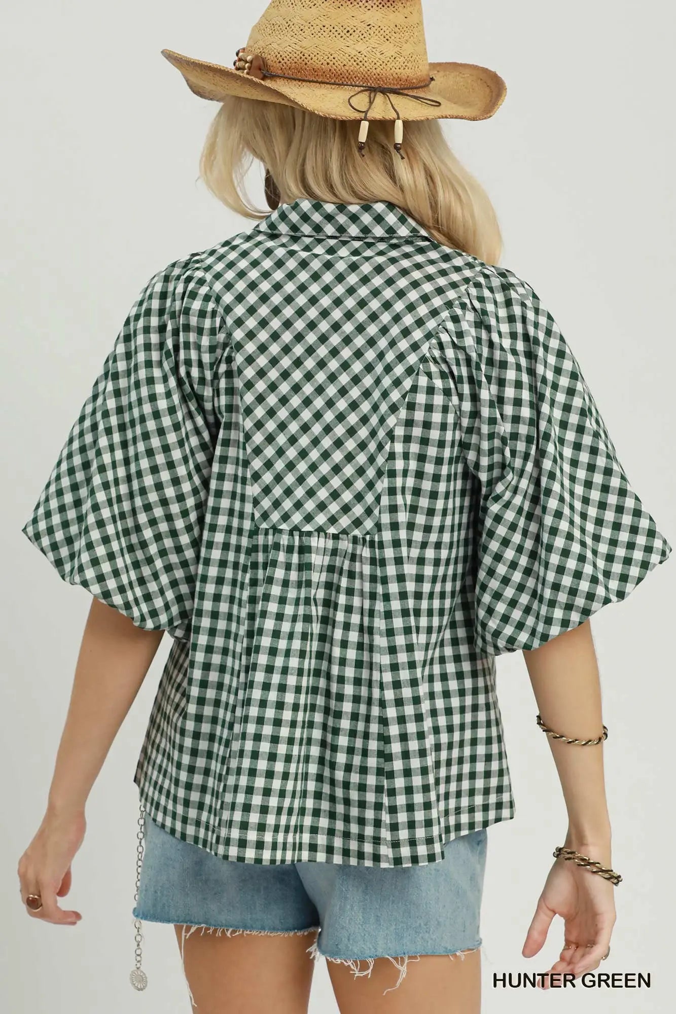 A woman shown from the back wearing a green and white gingham short-sleeve blouse with a gathered waist seam, paired with denim shorts and a straw hat. The color label 'HUNTER GREEN' is visible in the bottom right corner.