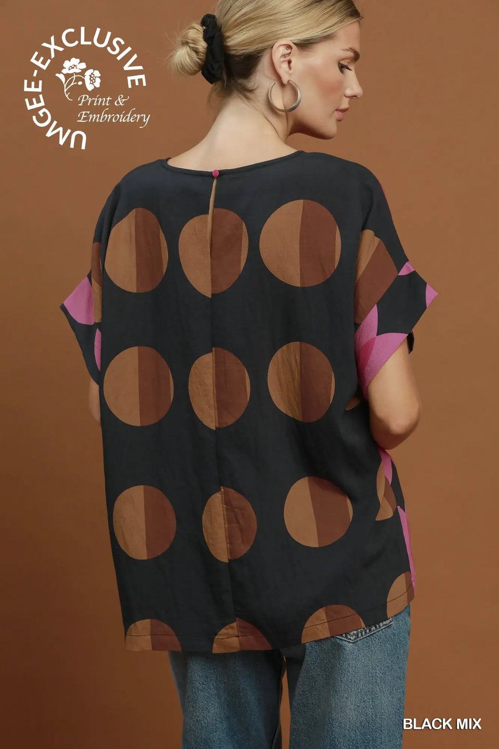 A woman shown from the back wearing a loose black blouse with large brown and tan polka dots and pink side panels, paired with blue jeans, against a warm brown studio background. A logo in the top left reads 'Unble - Exclusive Print & Embroidery' and 'BLACK MIX' appears in the bottom right.