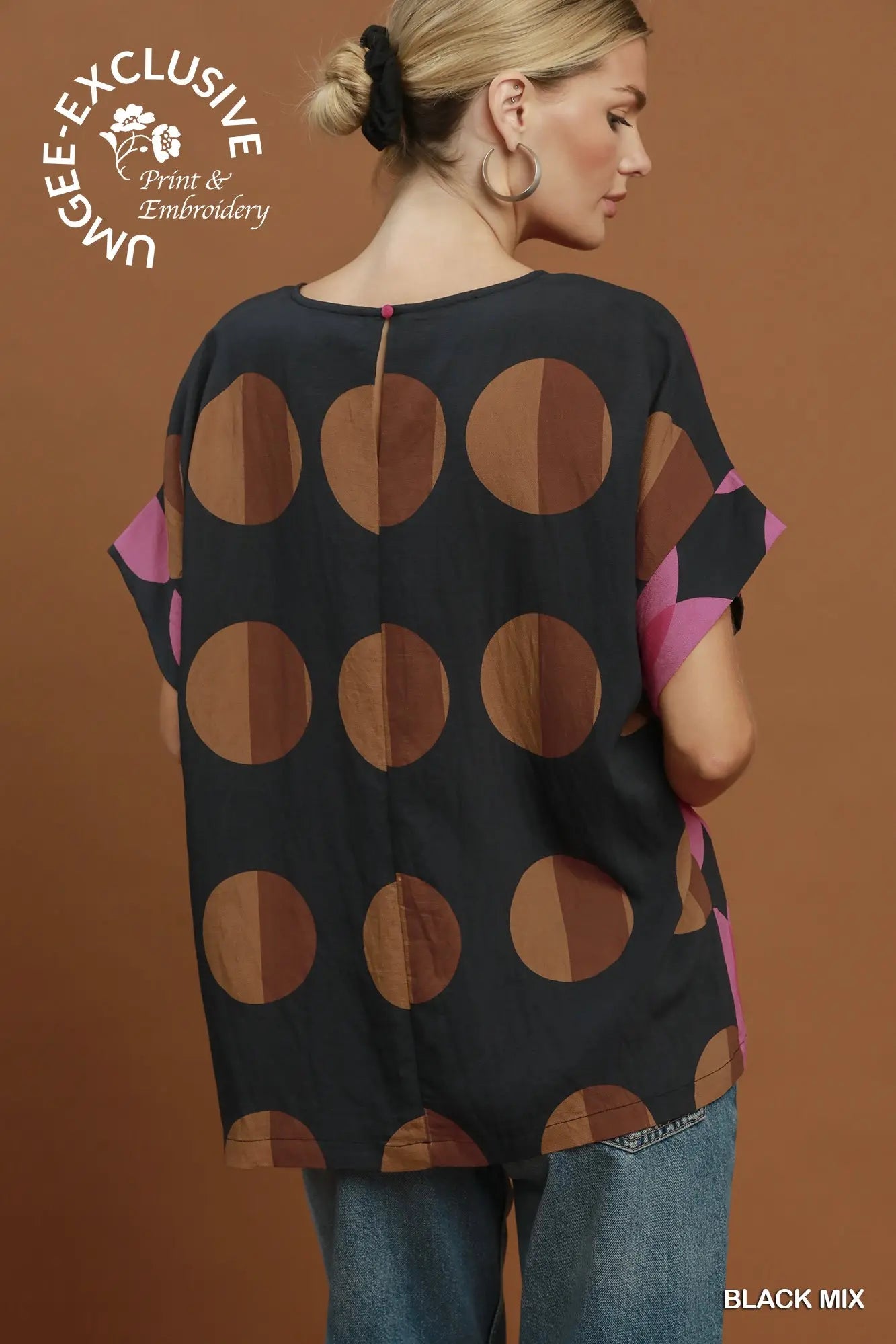 A woman shown from the back wearing a loose black blouse with large brown and tan polka dots and pink side panels, paired with blue jeans, against a warm brown studio background. A logo in the top left reads 'Unble - Exclusive Print & Embroidery' and 'BLACK MIX' appears in the bottom right.