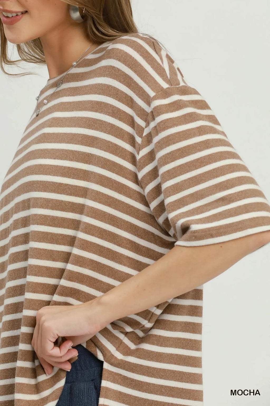 A close-up of a woman wearing an oversized short-sleeve knit top with horizontal brown and cream stripes, paired with dark blue jeans. The word 'MOCHA' is printed in the bottom right corner.