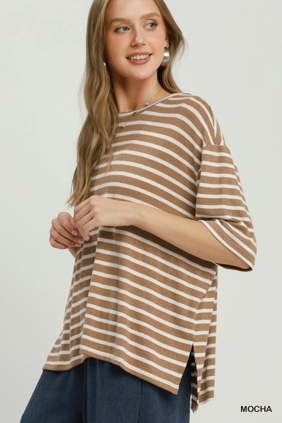 A woman wearing a brown and cream striped short-sleeve top with side slits, paired with dark blue pants, against a plain light background. The word 'MOCHA' is printed in the bottom right corner.