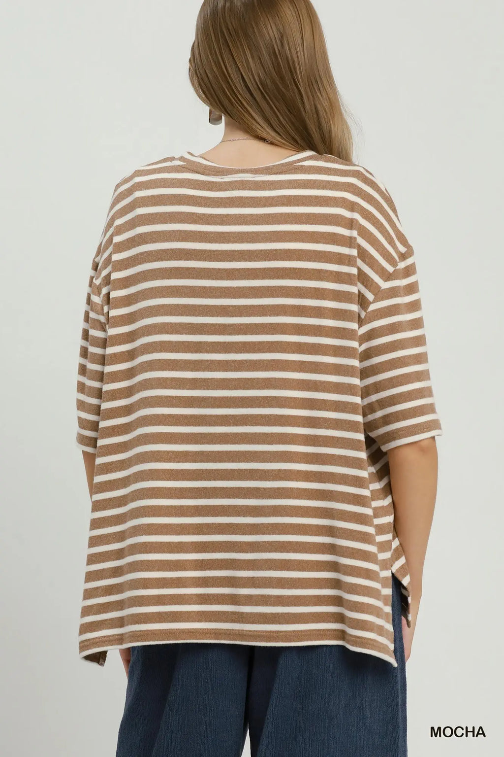 A woman shown from the back wearing an oversized short-sleeve striped top in brown and off-white, paired with dark blue pants, against a plain light gray background.