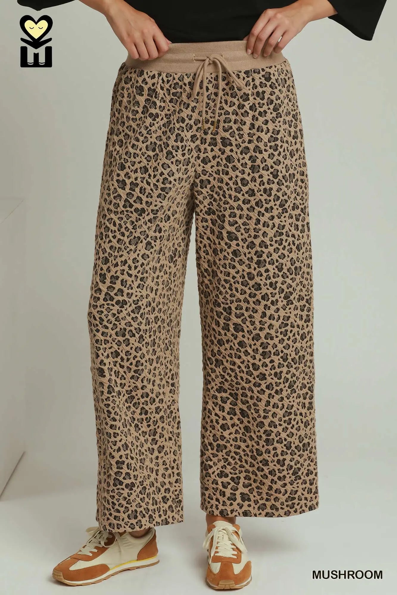 A person wearing loose, wide-leg drawstring pants in a beige and brown leopard print, paired with brown sneakers, shown from the waist down against a plain light background.