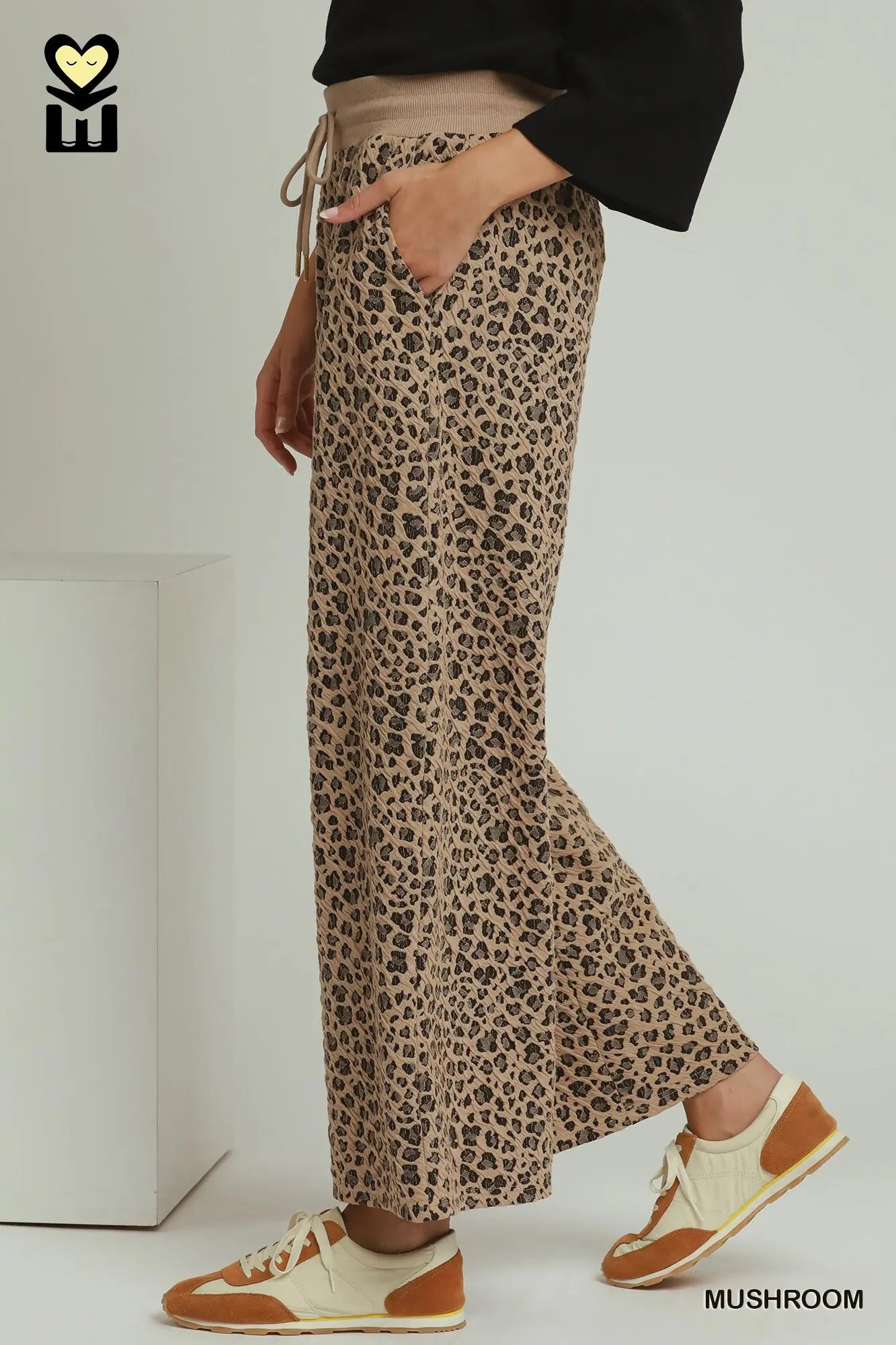 A person wearing wide-leg leopard-print pants with a beige waistband and tan sneakers, shown from the waist down in a studio setting. The word 'MUSHROOM' appears at the bottom right.