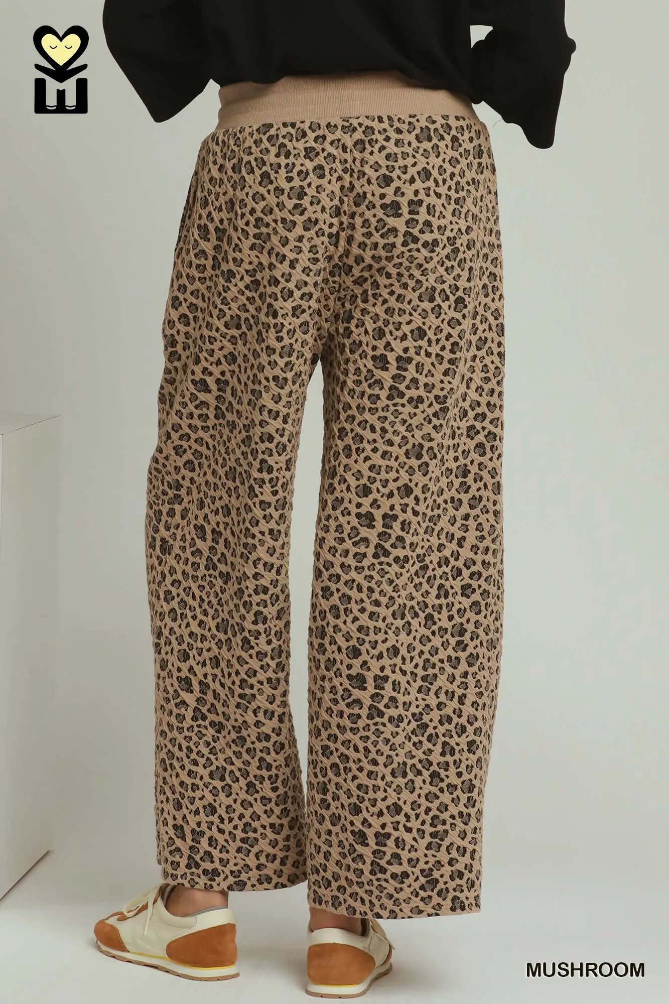 Wide-leg cropped pants in a brown and beige leopard print pattern, shown on a model from the back wearing a black top and white and brown sneakers.