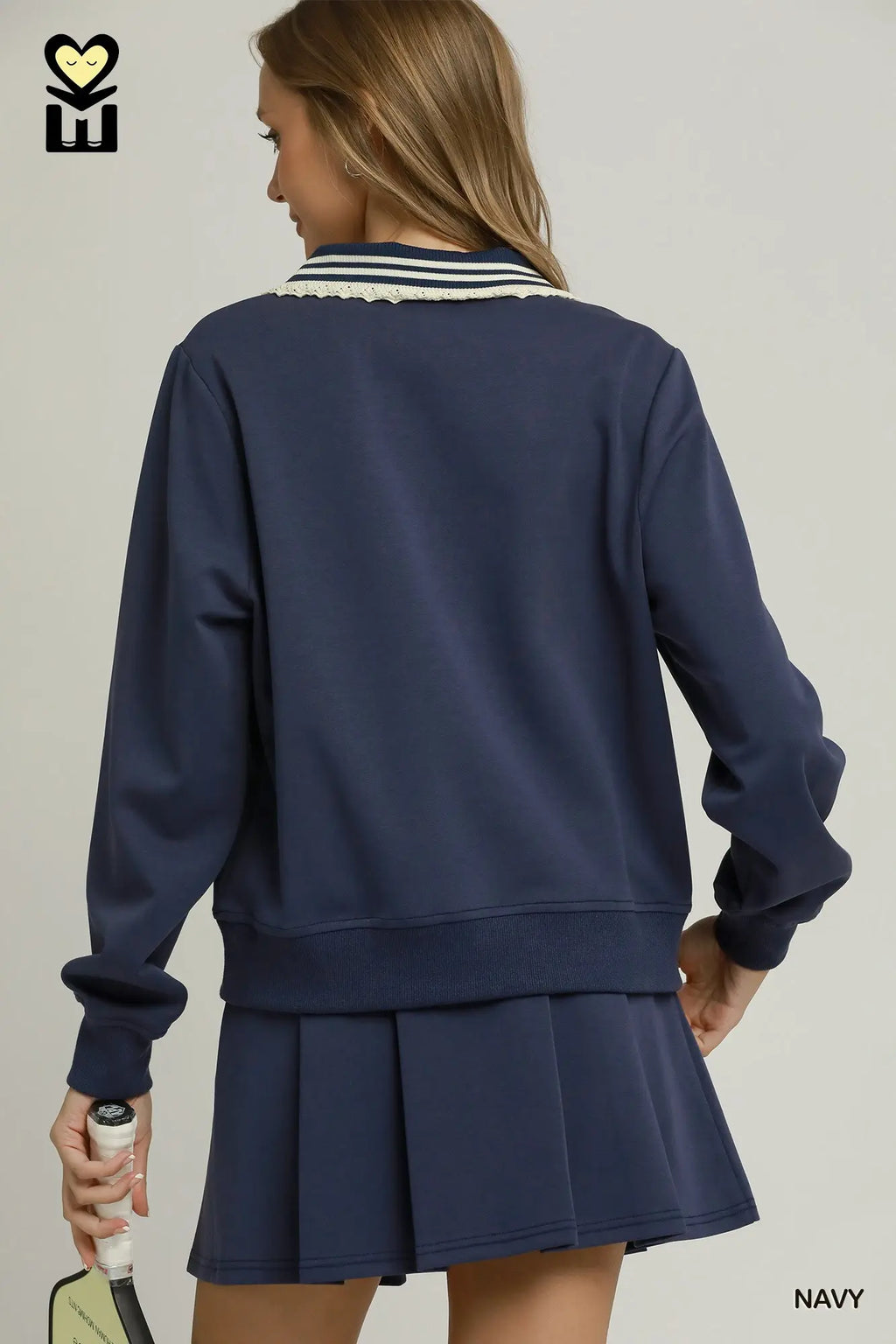 A woman shown from the back wearing a navy blue sweatshirt and matching pleated skirt set. The sweatshirt has a white and navy striped collar, and the image is set against a plain light gray studio background.