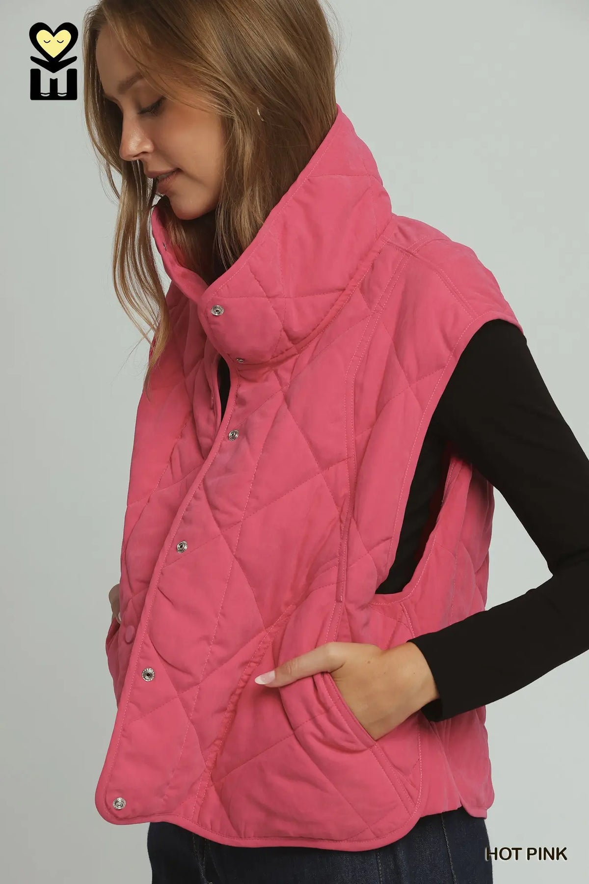 A woman wearing a quilted sleeveless puffer vest in hot pink over a black long-sleeve top, shown against a light gray studio background.