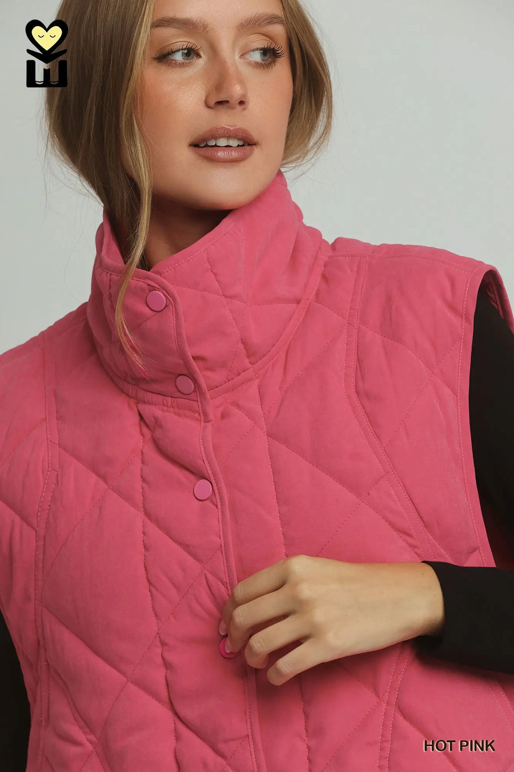 A woman wearing a quilted sleeveless puffer vest in hot pink, shown from the chest up against a light gray studio background. The vest has a high stand-up collar and front snap buttons.
