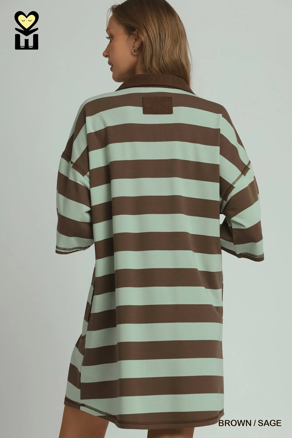 A woman shown from the back wearing an oversized short-sleeve collared shirt dress with horizontal brown and sage green stripes, against a light gray studio background.