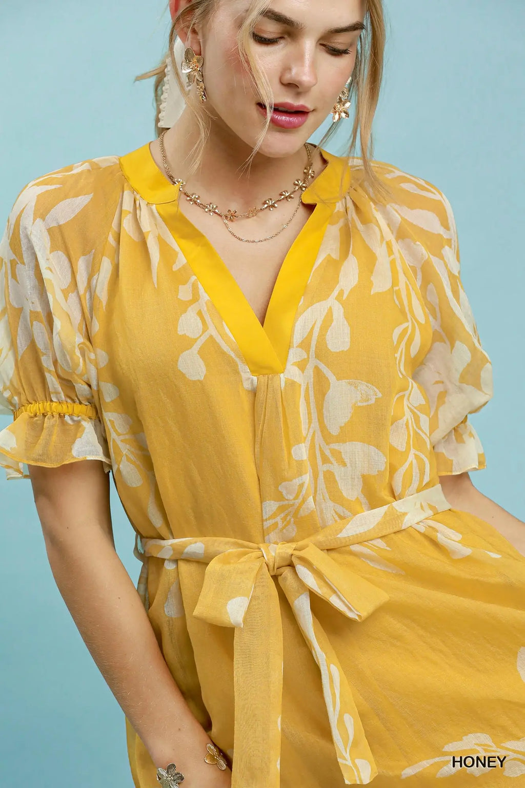 Woman wearing a yellow floral dress against a light blue background