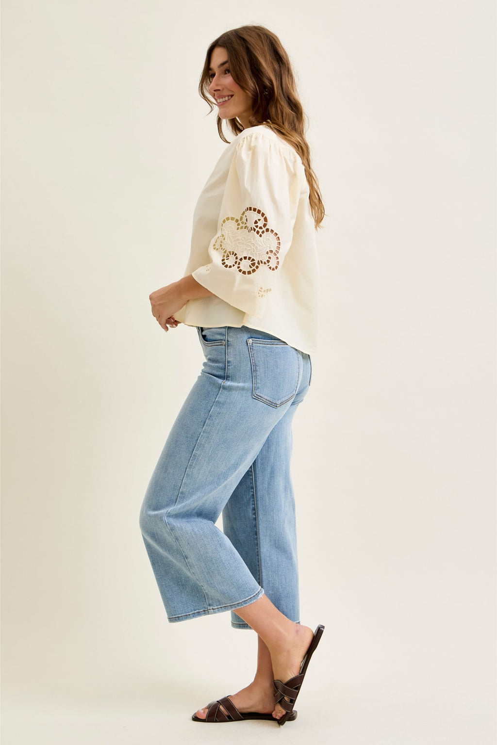 Woman wearing a cream sweater with floral embroidery and light blue jeans on a white background