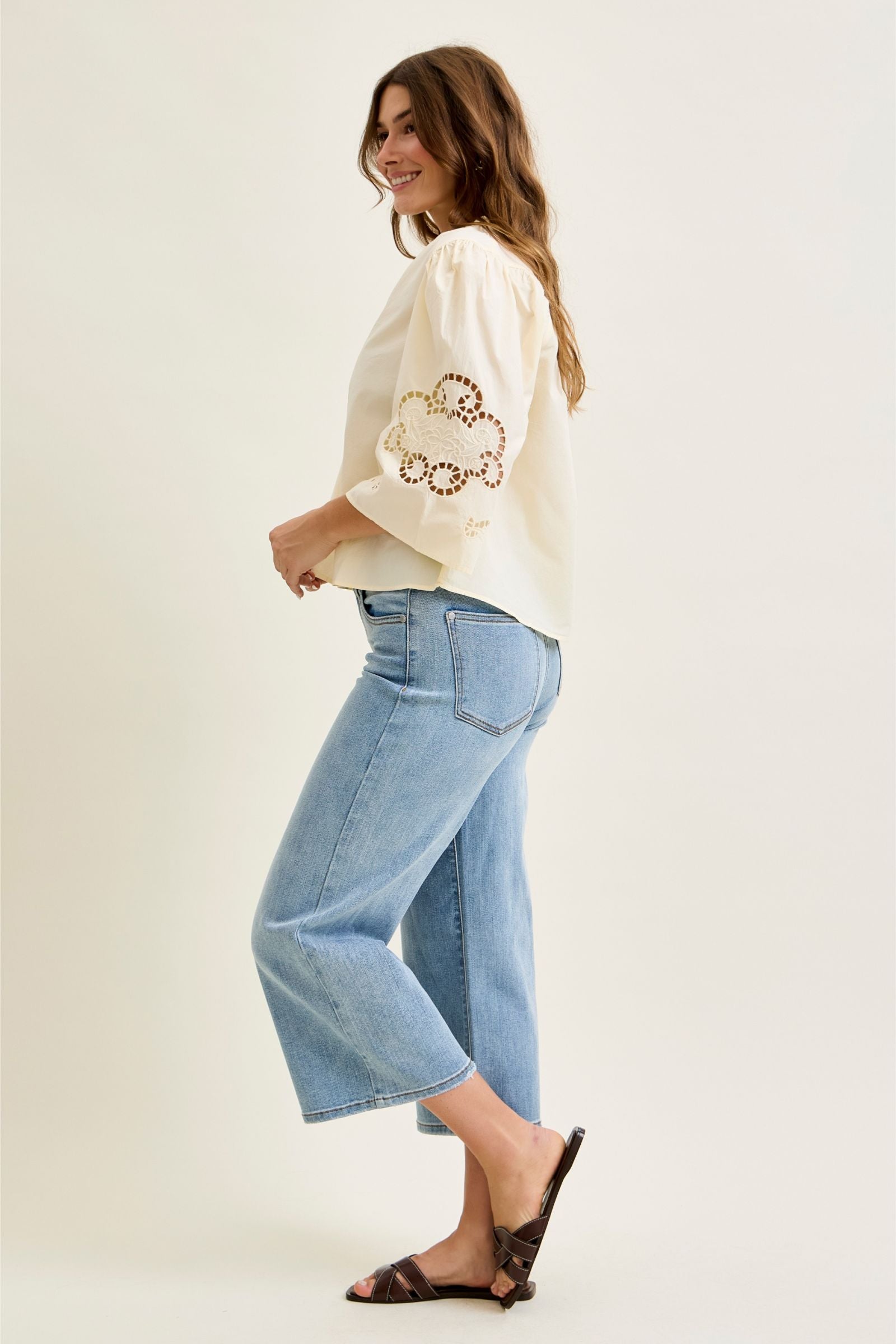 Woman wearing a cream sweater with floral embroidery and light blue jeans on a white background