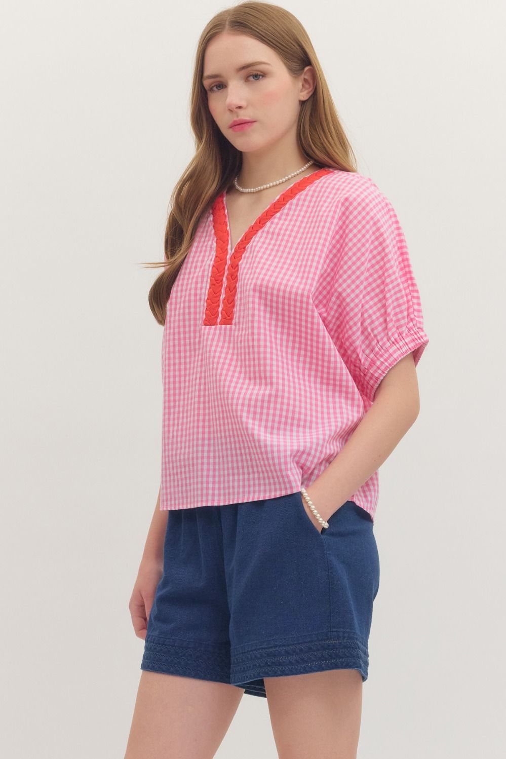 Woman wearing a pink checkered top with red trim and blue shorts on a white background