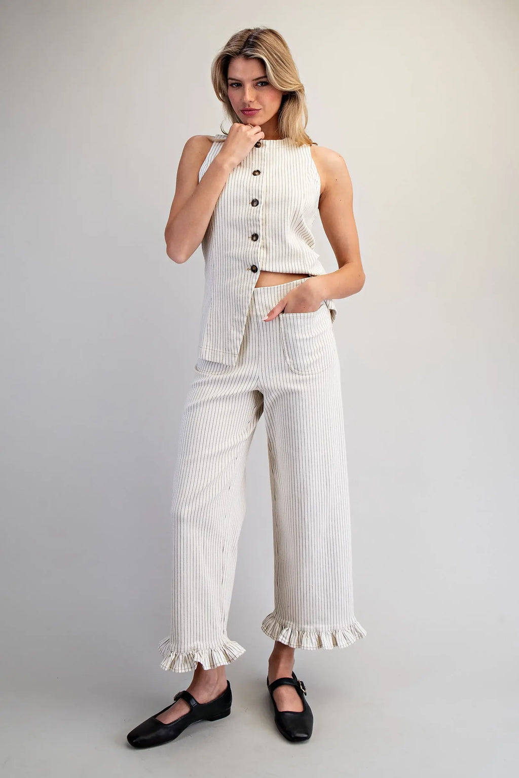 Woman wearing a white outfit with ruffled pants and black shoes on a plain background