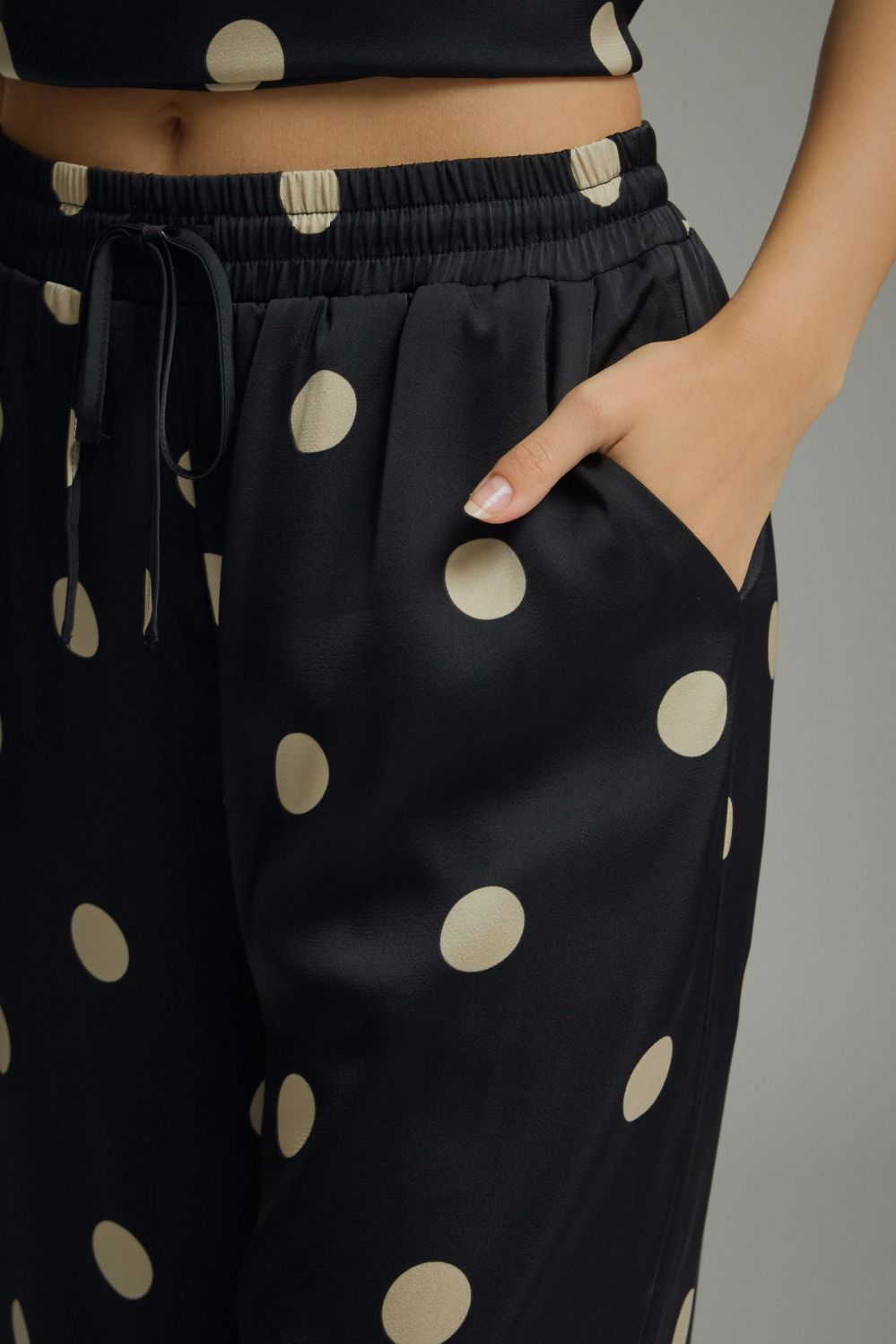 Black pants with beige polka dots worn by a person against a gray background