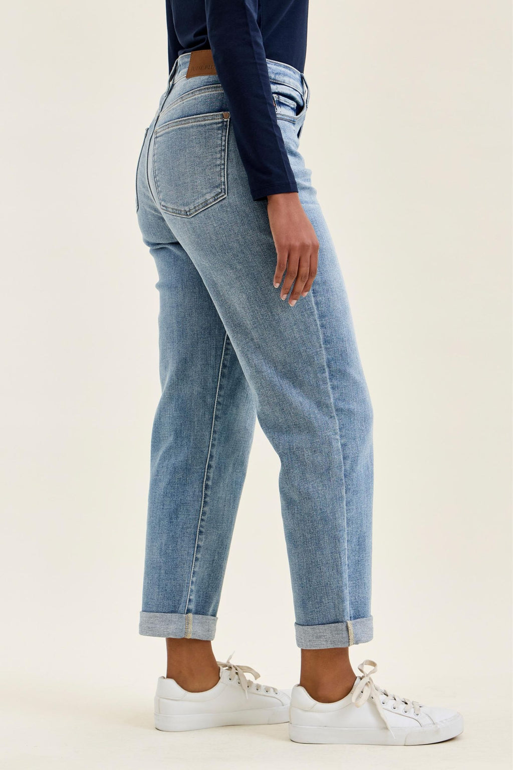 Person wearing light blue jeans and white sneakers on a plain background