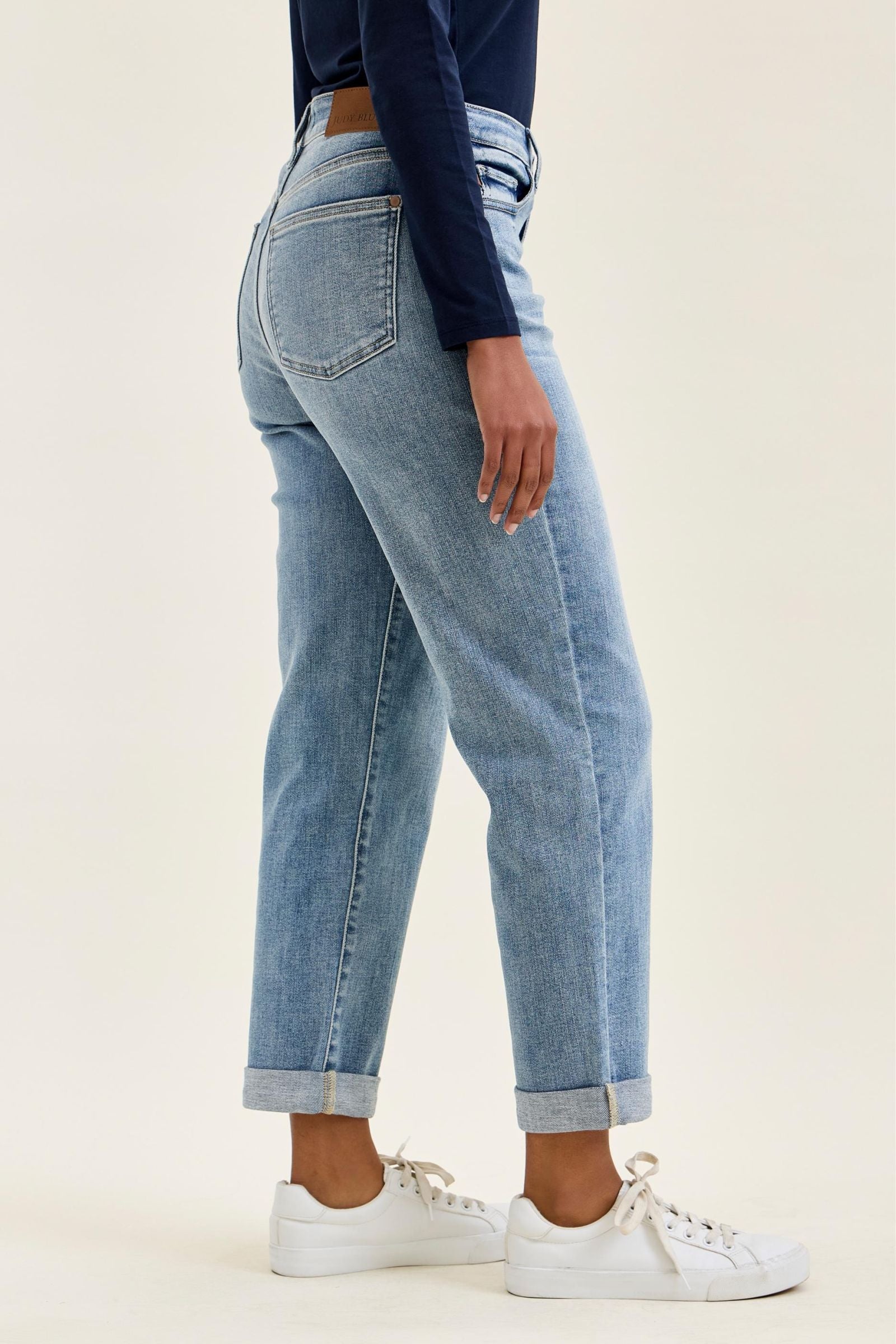 Person wearing light blue jeans and white sneakers on a plain background