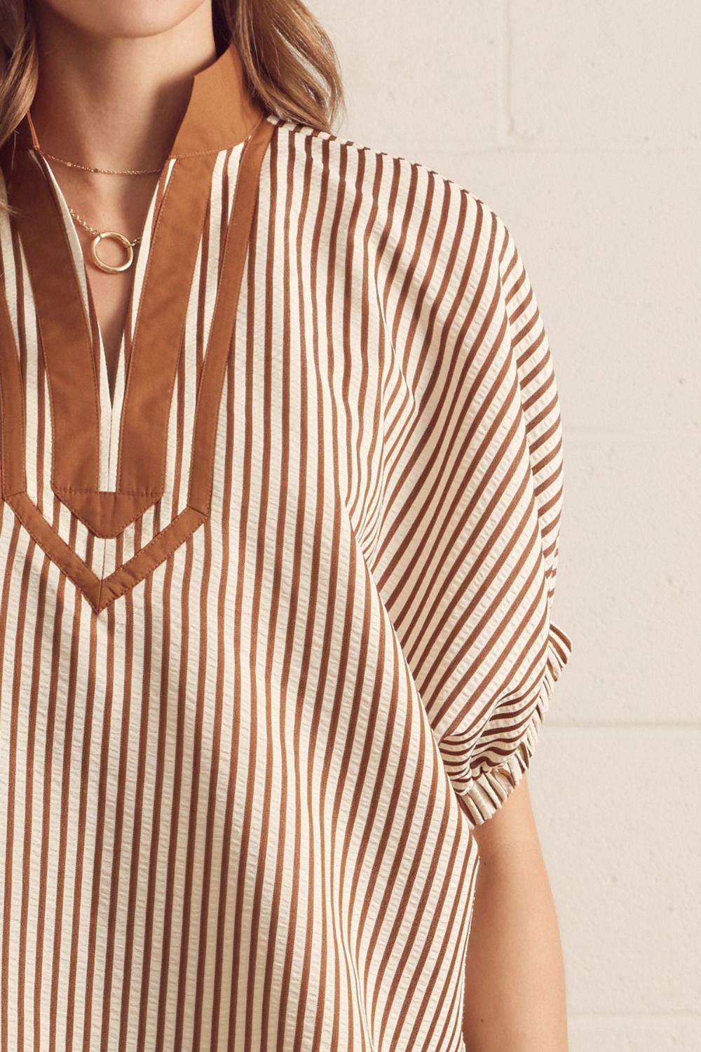 Close-up of a person wearing a brown and white striped shirt with a neutral background