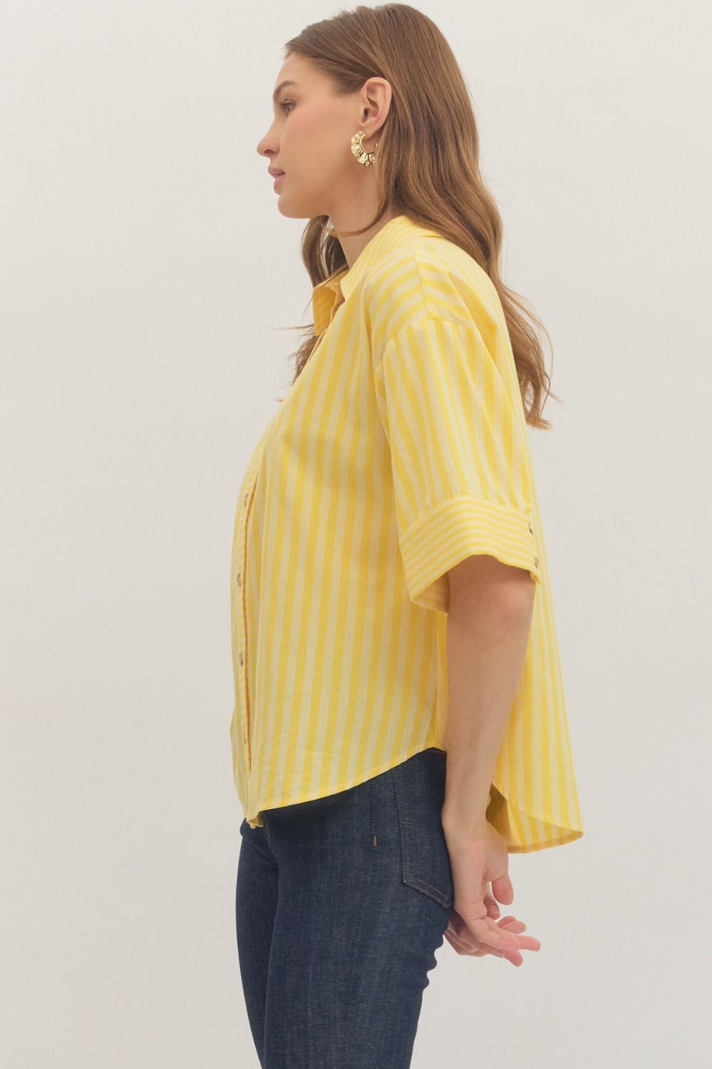 Woman wearing a yellow striped shirt and dark pants against a plain background