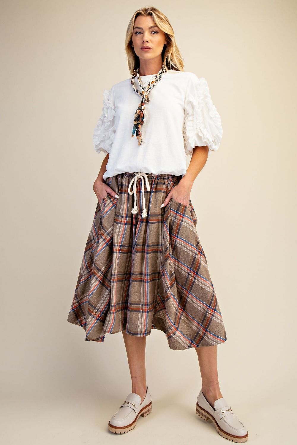 Woman wearing a white blouse and plaid skirt on a beige background