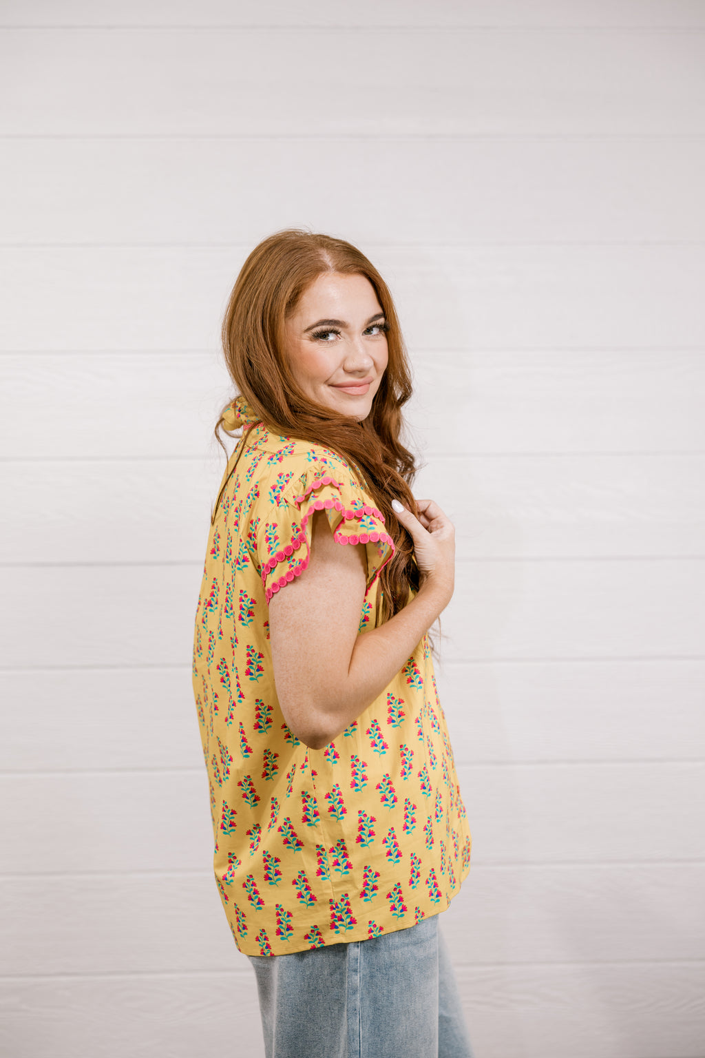 Woman wearing a yellow floral blouse against a white wall
