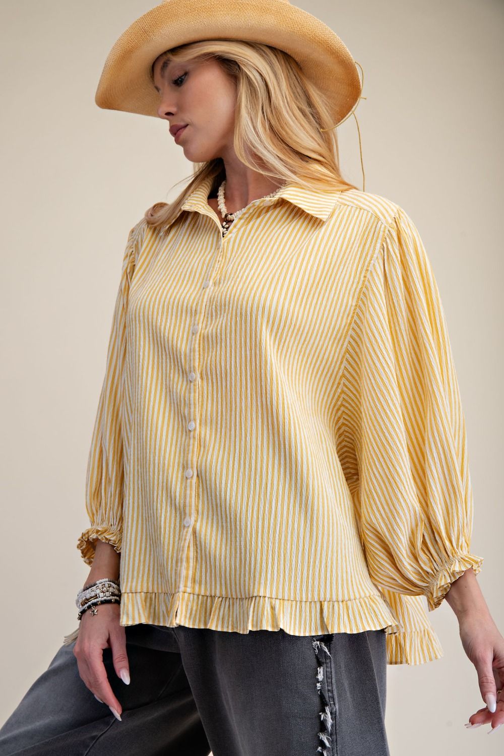 Woman wearing a yellow striped shirt and beige cowboy hat against a neutral background