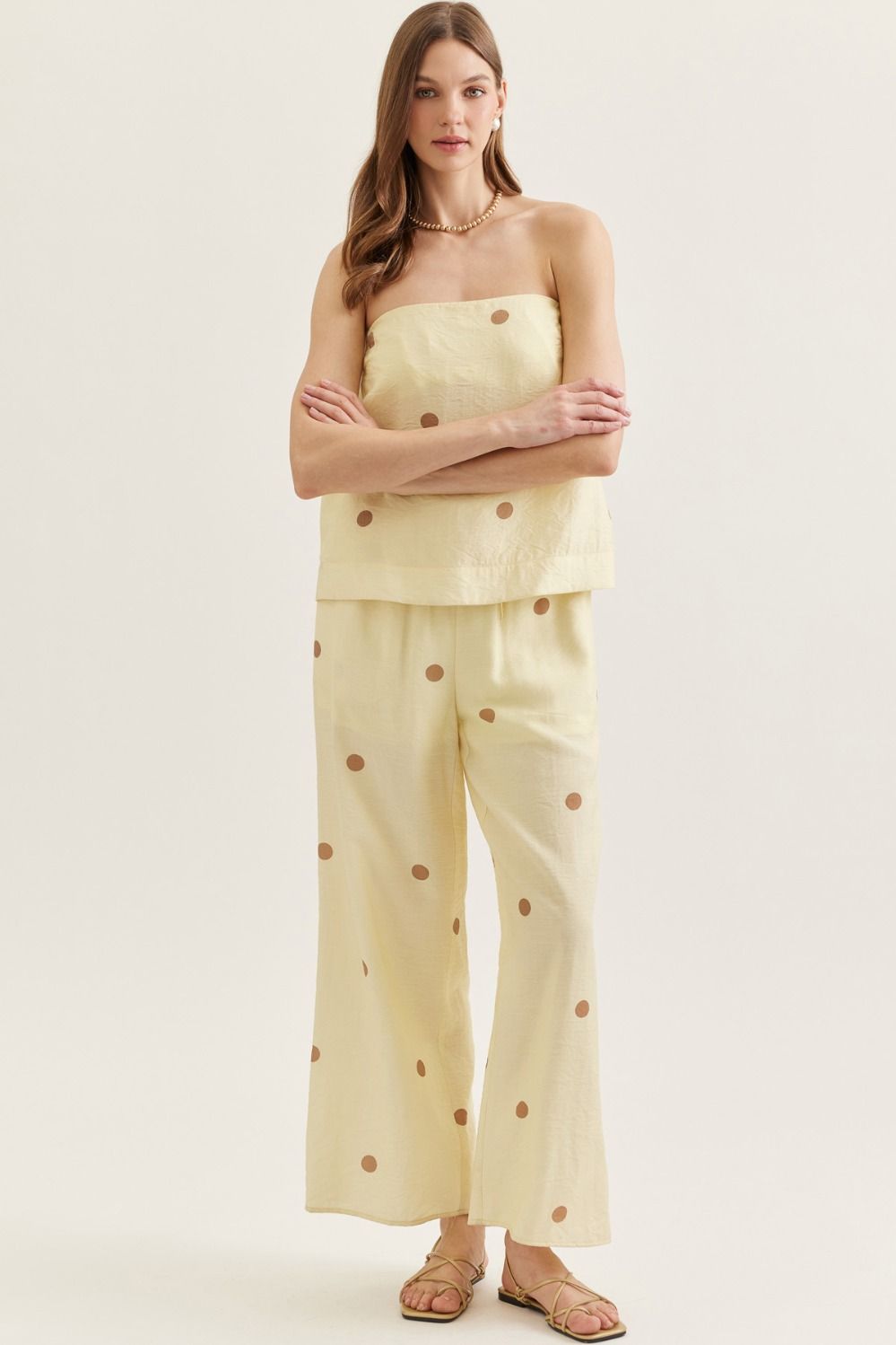 Woman wearing a light yellow strapless top and wide-leg pants with brown polka dots on a white background
