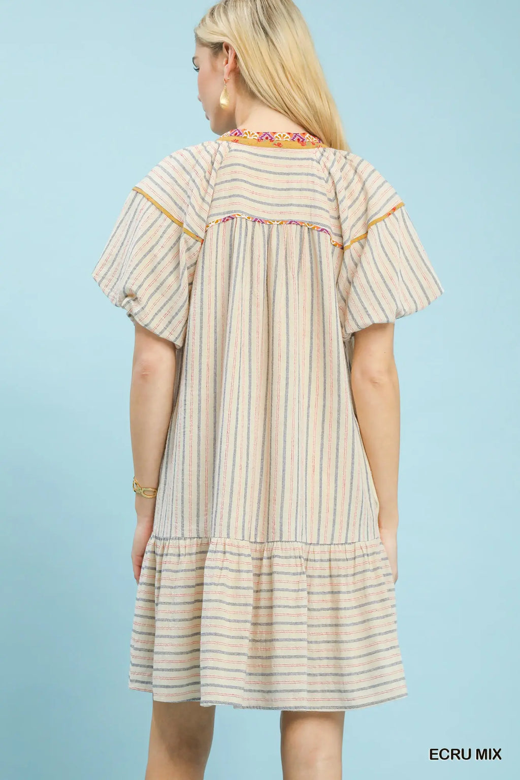 Woman wearing a striped dress with embroidered details on a light blue background
