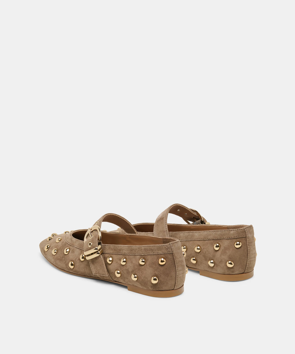 A pair of taupe-brown suede Mary Jane flats decorated with gold-tone metal studs and buckle straps, shown from a side-rear angle on a light gray background.