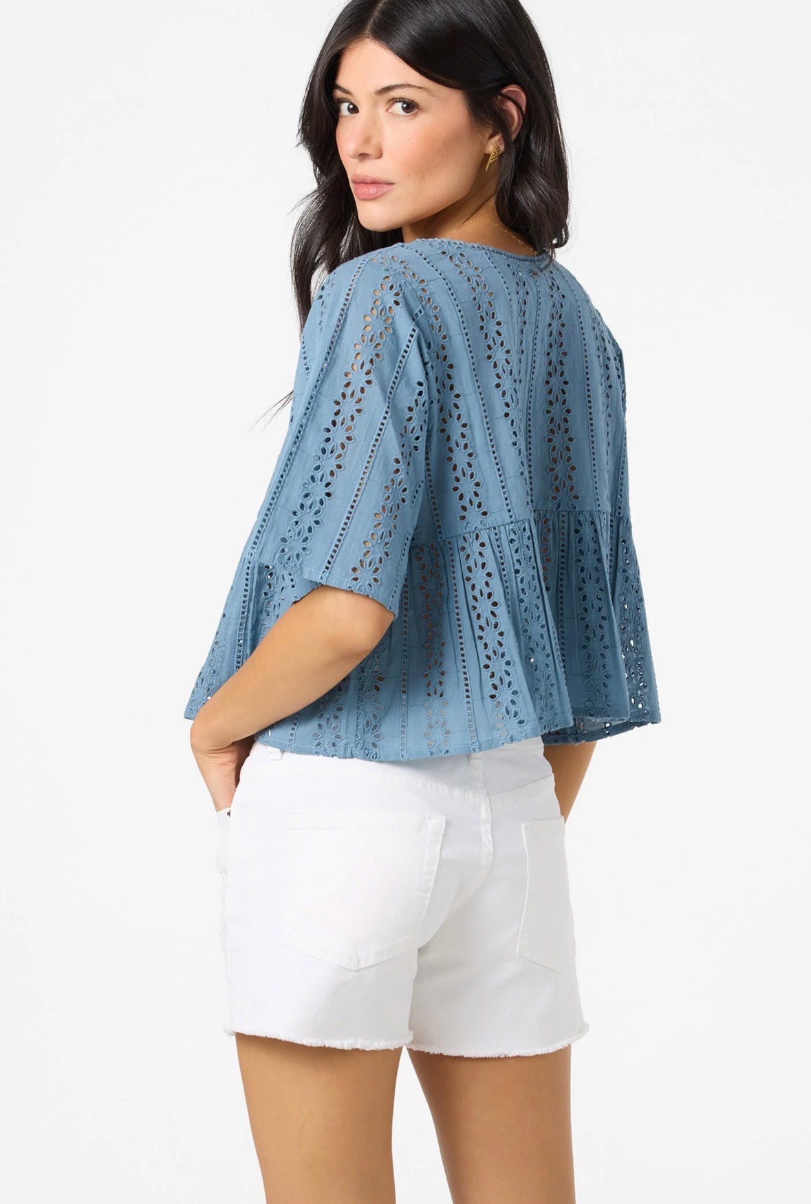 Woman wearing a blue lace top and white shorts on a white background