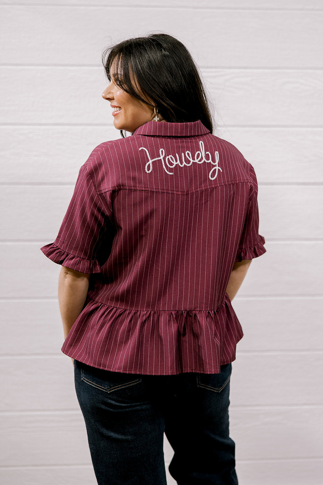 Woman wearing a maroon ruffled shirt with 'Howdy' embroidered on the back against a white background