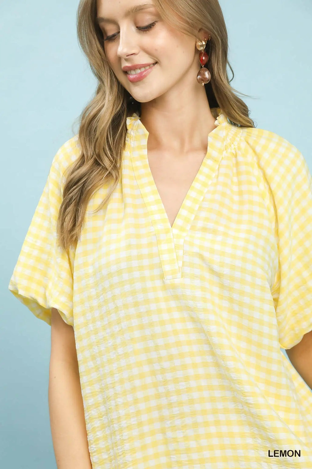 Woman wearing a yellow checkered blouse against a light blue background