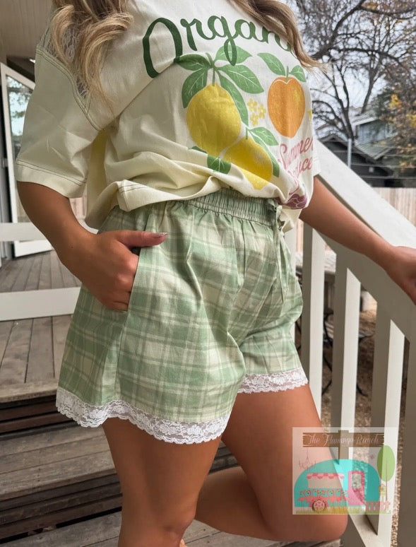 Person wearing a white t-shirt with fruit graphics and green plaid shorts on a wooden deck.