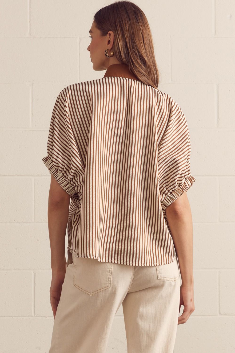 Woman wearing a striped shirt and beige pants against a light background