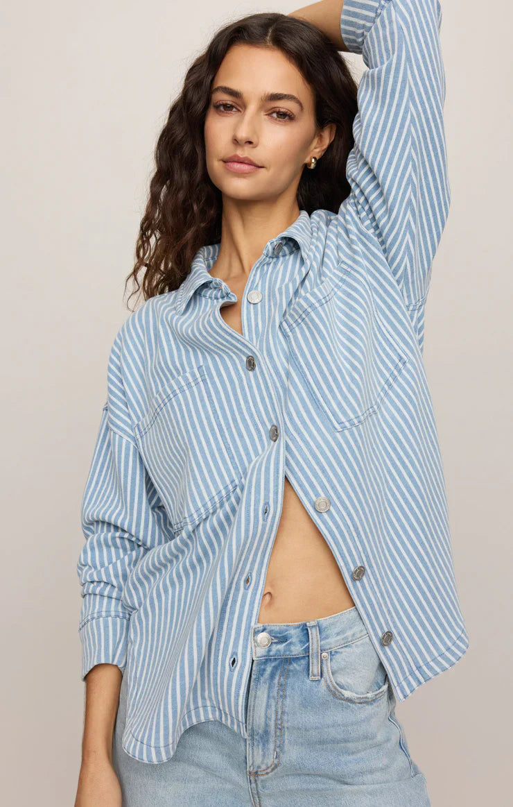 Woman wearing a blue and white striped shirt with rolled-up sleeves against a beige background