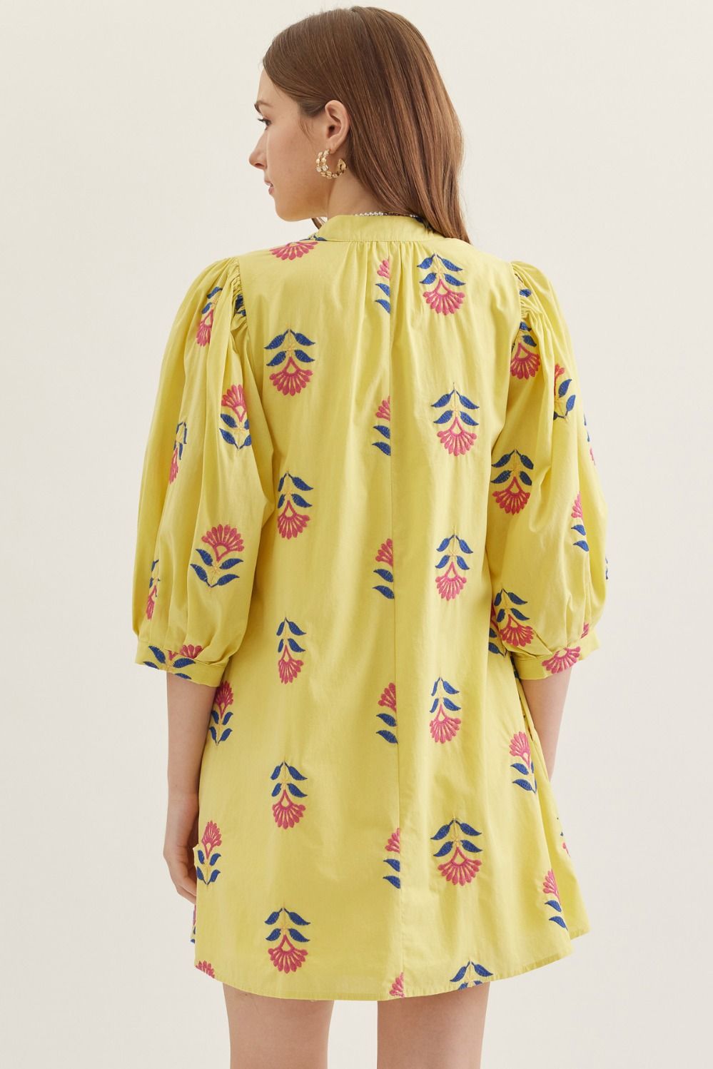 Woman wearing a yellow dress with floral patterns on a plain background