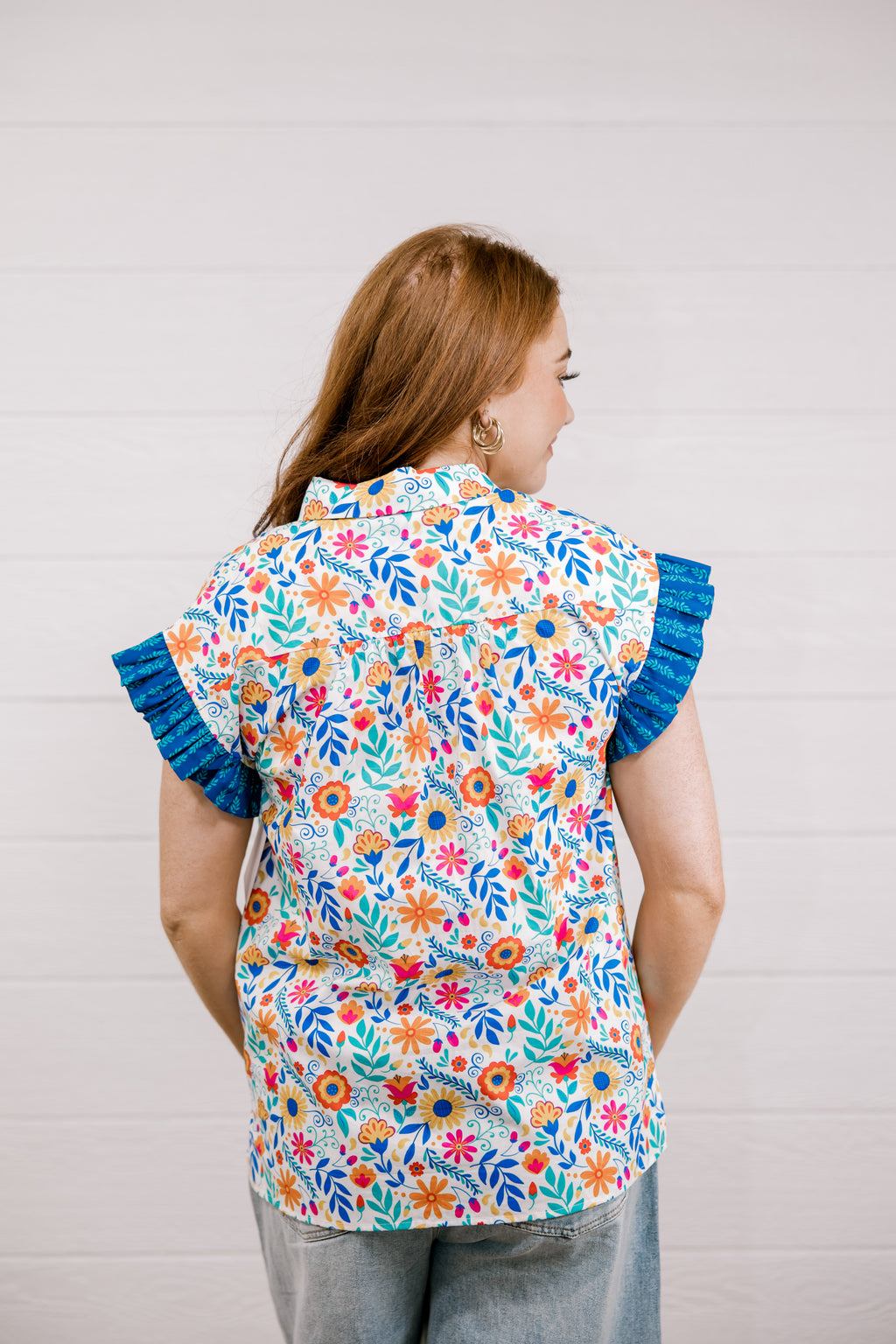 Woman wearing a colorful floral blouse with blue ruffled sleeves against a plain background