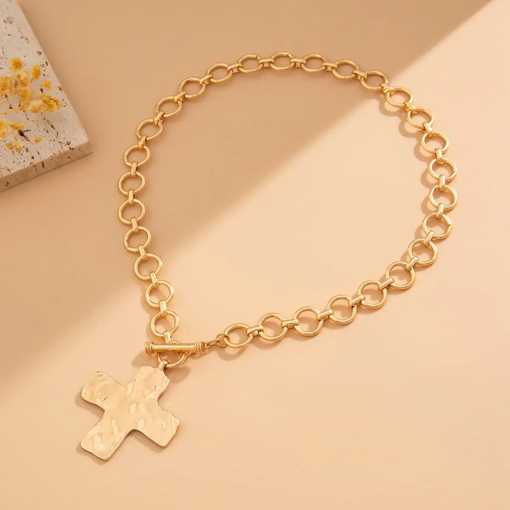 Gold chain bracelet with a cross pendant on a beige background
